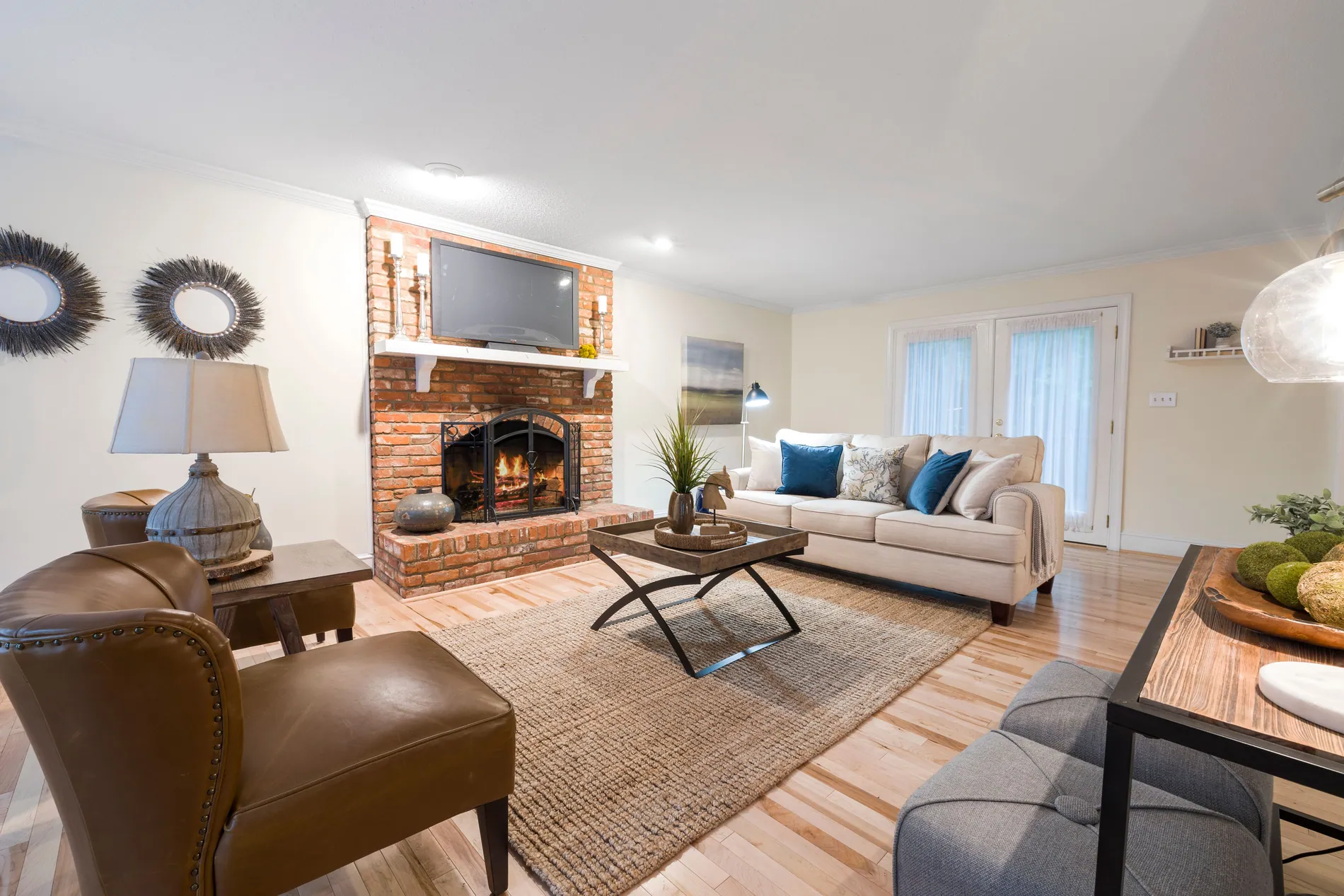 Bright living room with a red brick fireplace, empty before and with a warm fire added by Stager AI after