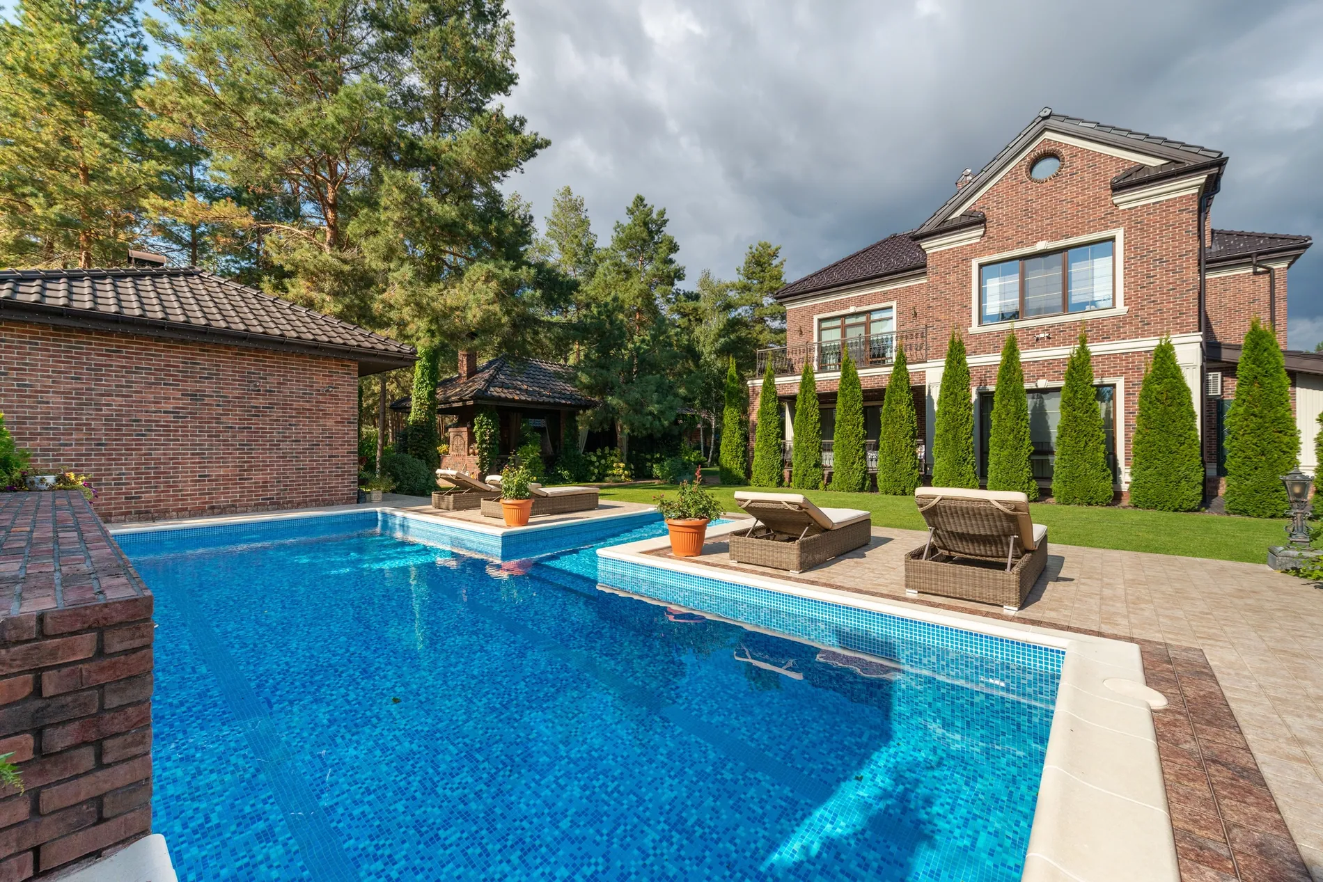 Brick house and pool under a heavy grey sky, replaced by a deep blue sky with soft clouds
