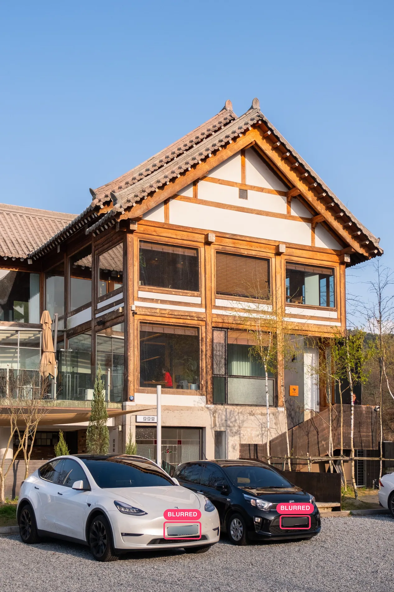 Timber house with two cars parked in front, front license plates blurred by Stager AI