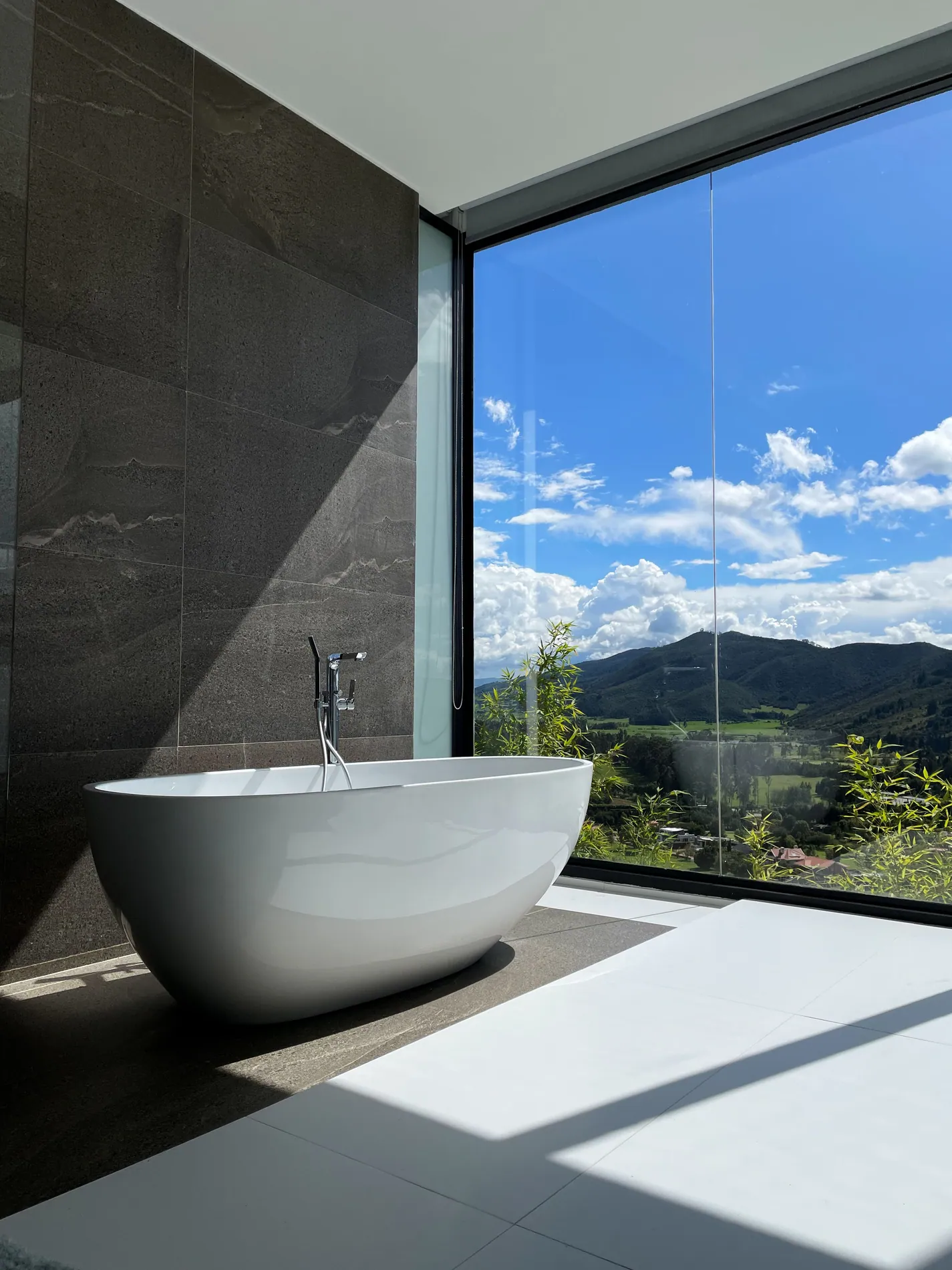 Bathroom with a freestanding tub and a floor-to-ceiling window showing a sharp mountain view, edited by Stager AI